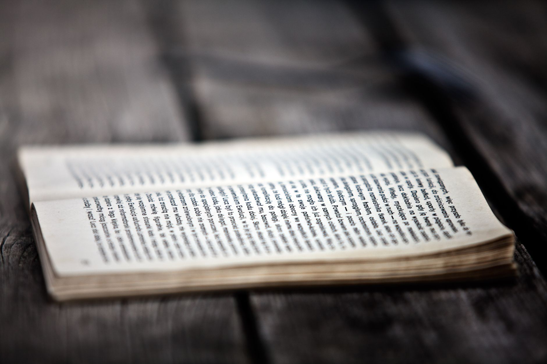 Un livre ouvert posé sur une table en bois sombre, dans une lumière rasante