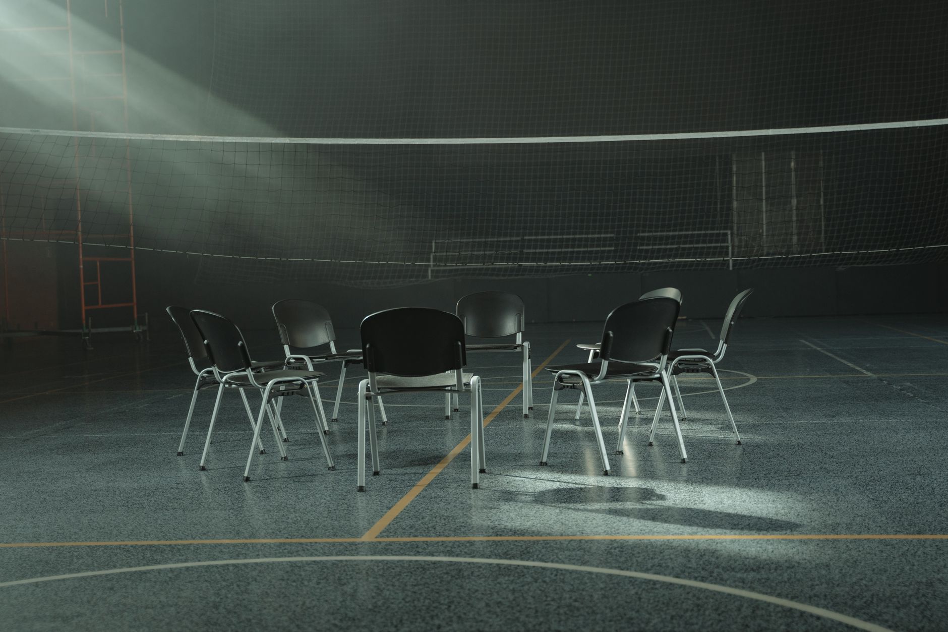 Des chaises disposées en cercle dans un gymnase vide, éclairées par une lumière rasante